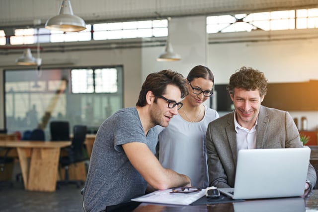 Drei Fachleute begutachten lachend 'Sage 100' Rechnungswesen-Software auf einem Laptop in einem modernen Büro, reflektiert Teamarbeit und Finanzanalyse in der Schweiz.