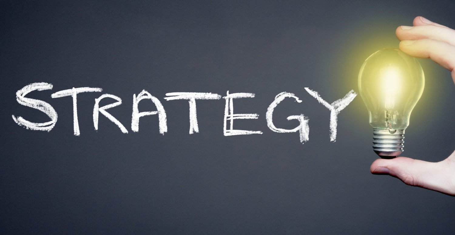 Strategie Konzept mit Glühbirne – Wort „Strategy“ in Kreideschrift und leuchtende Glühbirne als Symbol für Innovation