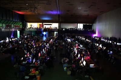 Eine Turnhalle mit vielen Tischen und Personen die daran Videogame spielen.