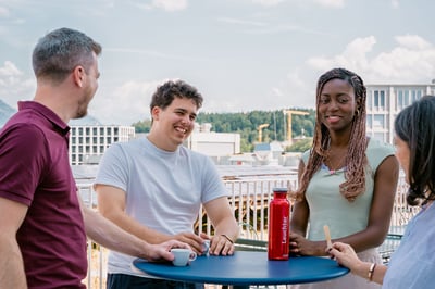 Vier Kolleginnen und Kollegen im lockeren Austausch auf einer Dachterrasse.