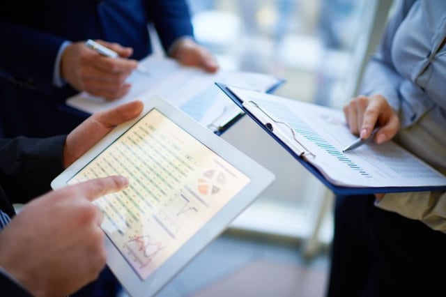 Wirtschaftsfachleute analysieren Finanzberichte auf einem Tablet mit 'Sage 100' Software, symbolisch für fortschrittliches Rechnungswesen in der Schweiz.