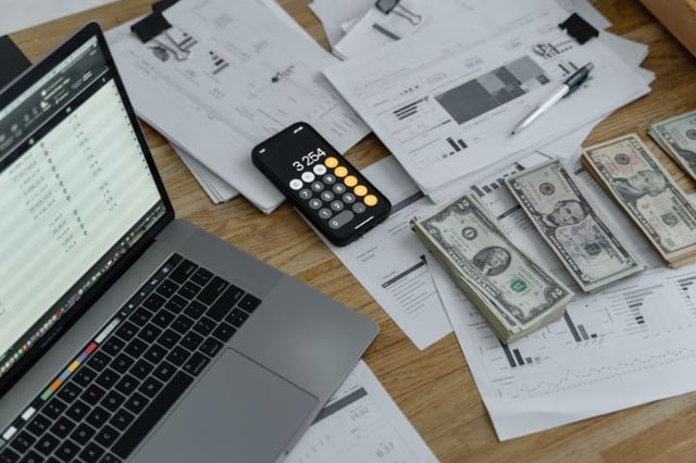Arbeitsplatz mit Laptop, der 'Sage 100' für Rechnungswesen anzeigt, umgeben von Finanzunterlagen, Bargeld und einem Taschenrechner, symbolisiert effektives Finanzmanagement in der Schweiz.