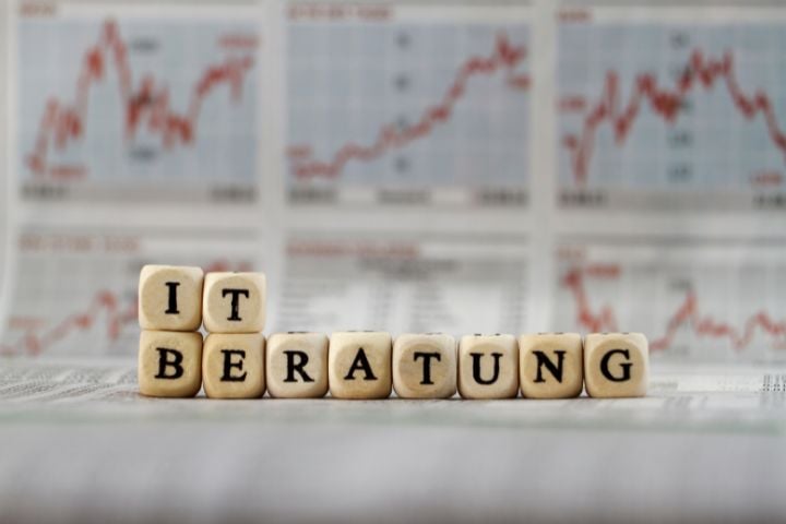 IT-Beratung mit Holzbuchstaben vor Börsendiagrammen und Aktienkursen