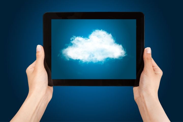 Eine Person hält ein Tablet in der Hand und darauf ist eine Wolke mit blauem Hintergrund zu sehen.