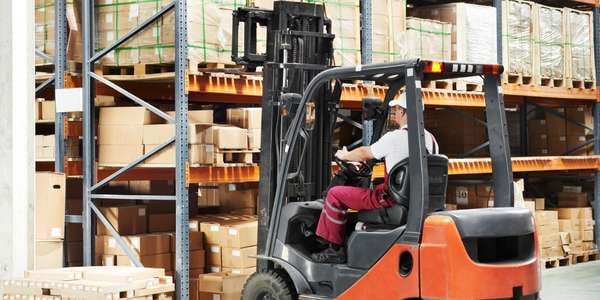 Logistikmitarbeiter fährt Gabelstapler im modernen Lagerhaus mit Hochregalen