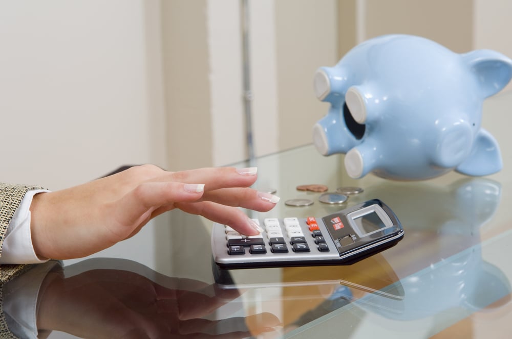Womans hands on calculator with piggy bank in background.-1