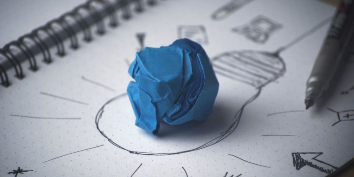 Kreativitätsprozess Illustration – zerknülltes blaues Papier auf Skizze einer Glühbirne im Notizbuch