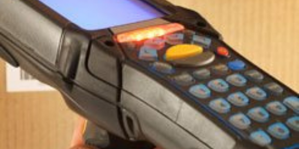 Barcode Scanner im Lager – mobiler Handscanner mit Display und Tastatur vor Kartonhintergrund
