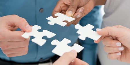 Vier Hände, die weiße Puzzleteile halten und zusammenfügen, symbolisch für Teamarbeit und Zusammenarbeit, in einem Schweizer Unternehmenskontext.