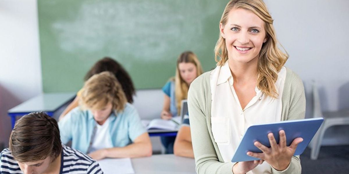 Lehrerin mit Tablet im Klassenzimmer – digitaler Unterricht mit Schülern im Hintergrund