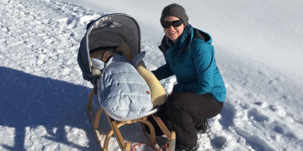 Winterspaziergang mit Baby im Schlitten und Kinderwagenaufsatz in verschneiter Schweizer Berglandschaft