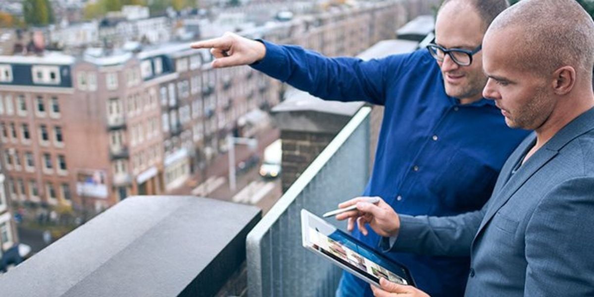 Geschäftsgespräch mit Tablet auf Dachterrasse – zwei Männer analysieren digitale Inhalte mit Stadtblick im Hintergrund