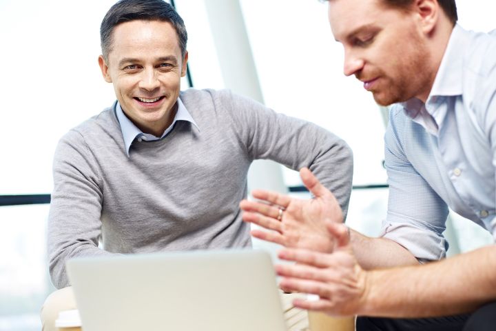 Zwei Geschäftsleute diskutieren lächelnd über Rechnungswesen-Strategien auf einem Laptop, möglicherweise mit 'Sage 100' Software, in einem hellen Büro in der Schweiz.