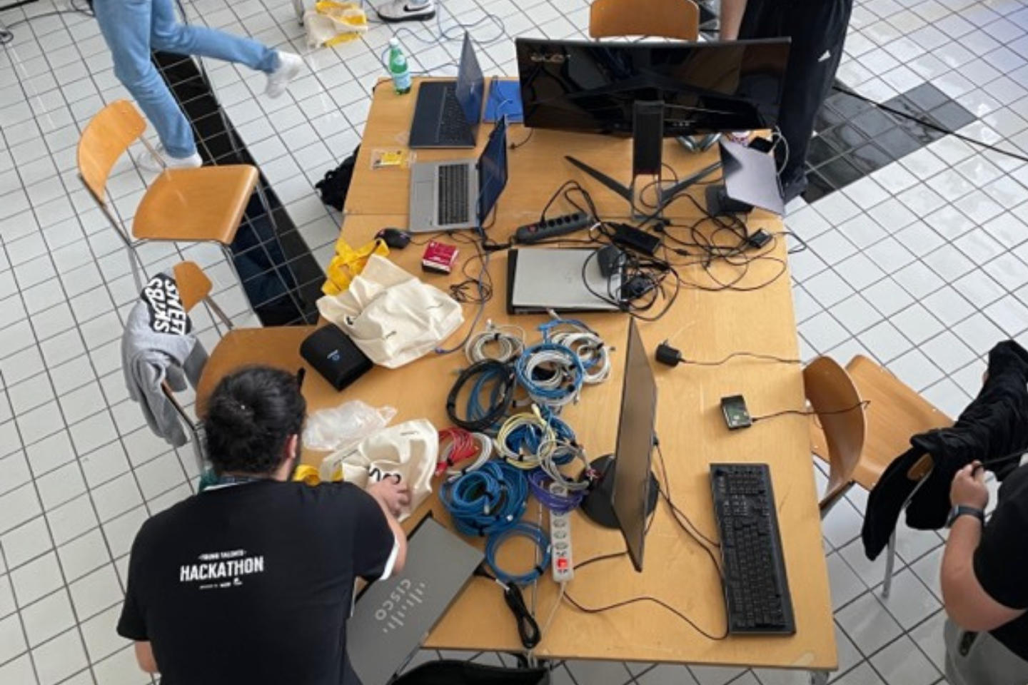 Teilnehmer am 'Young Talents Hackathon' in der Schweiz arbeiten an einem voll ausgestatteten Entwicklertisch mit Laptops und Elektronikbauteilen.